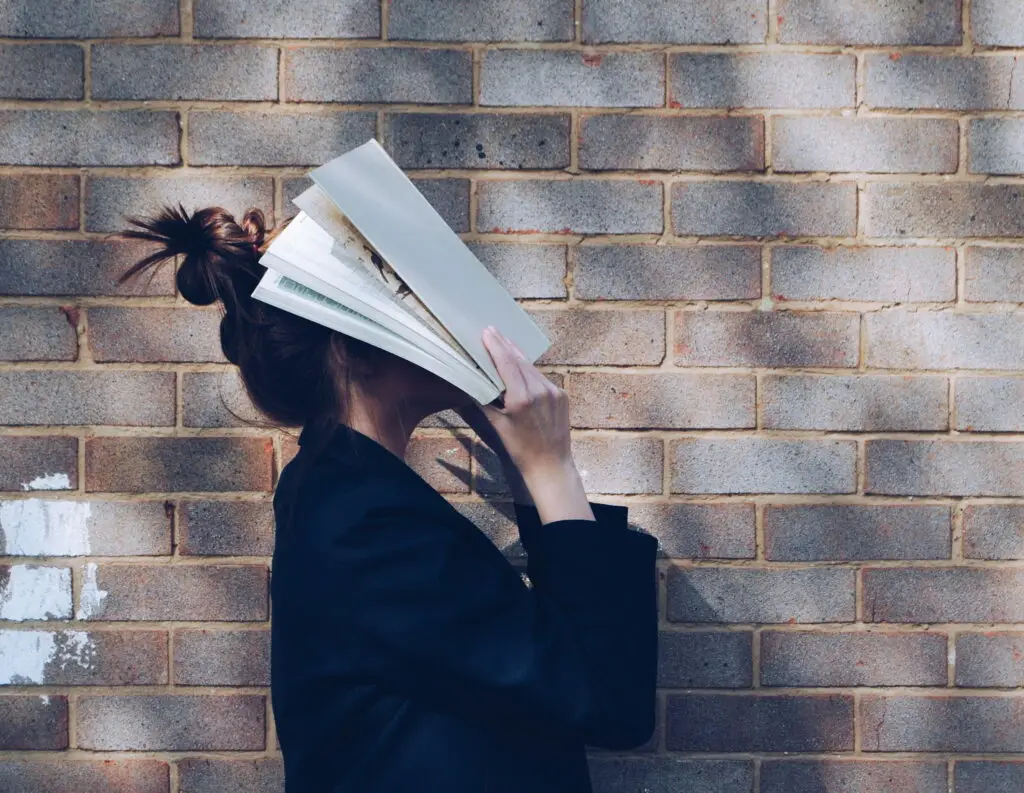 Female student with an open book held against her head, obscuring her face