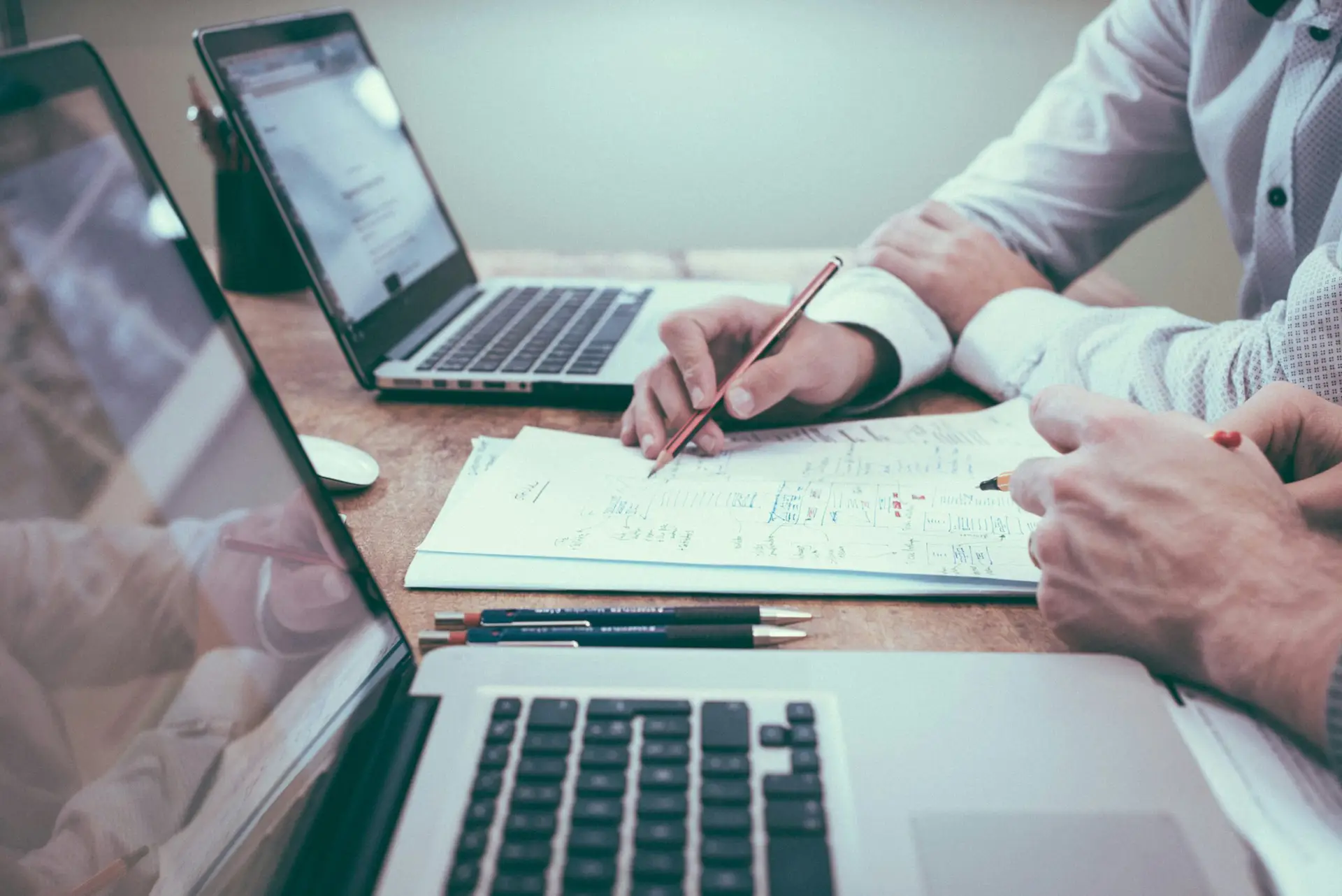 Two laptops with two people working on a piece of paper between them